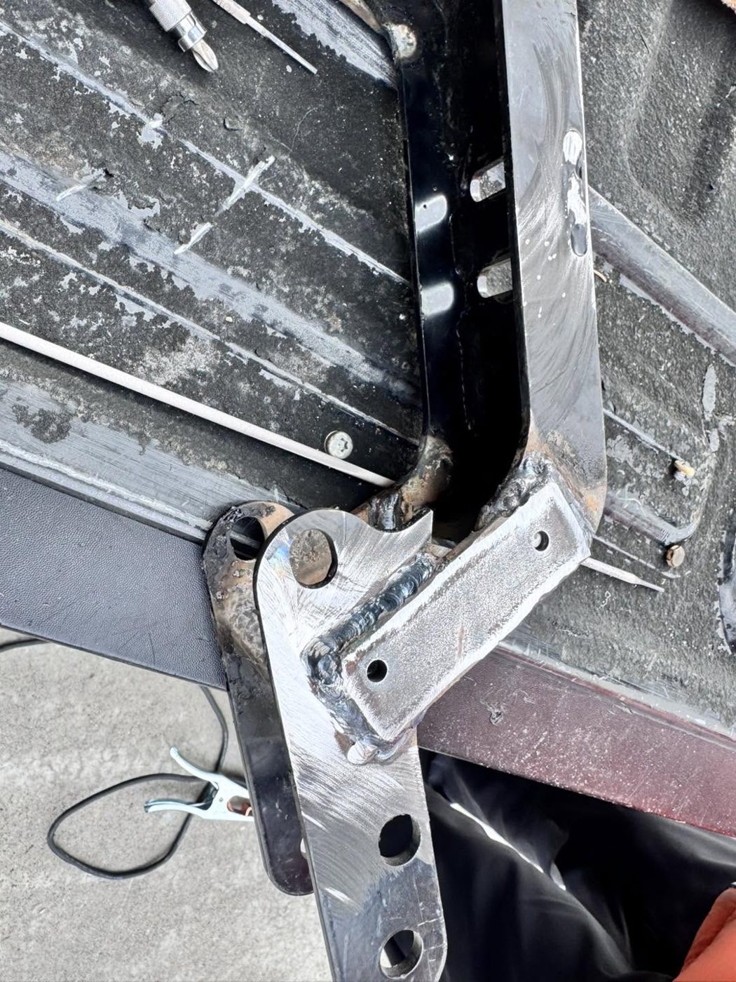 A bent steel bracket clamped on a steel work surface, with fresh welds at the joints