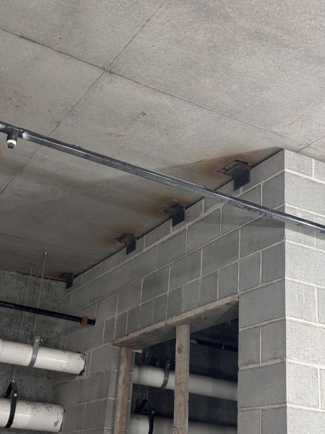 Steel angle clips welded to the concrete ceiling along the top of a block wall