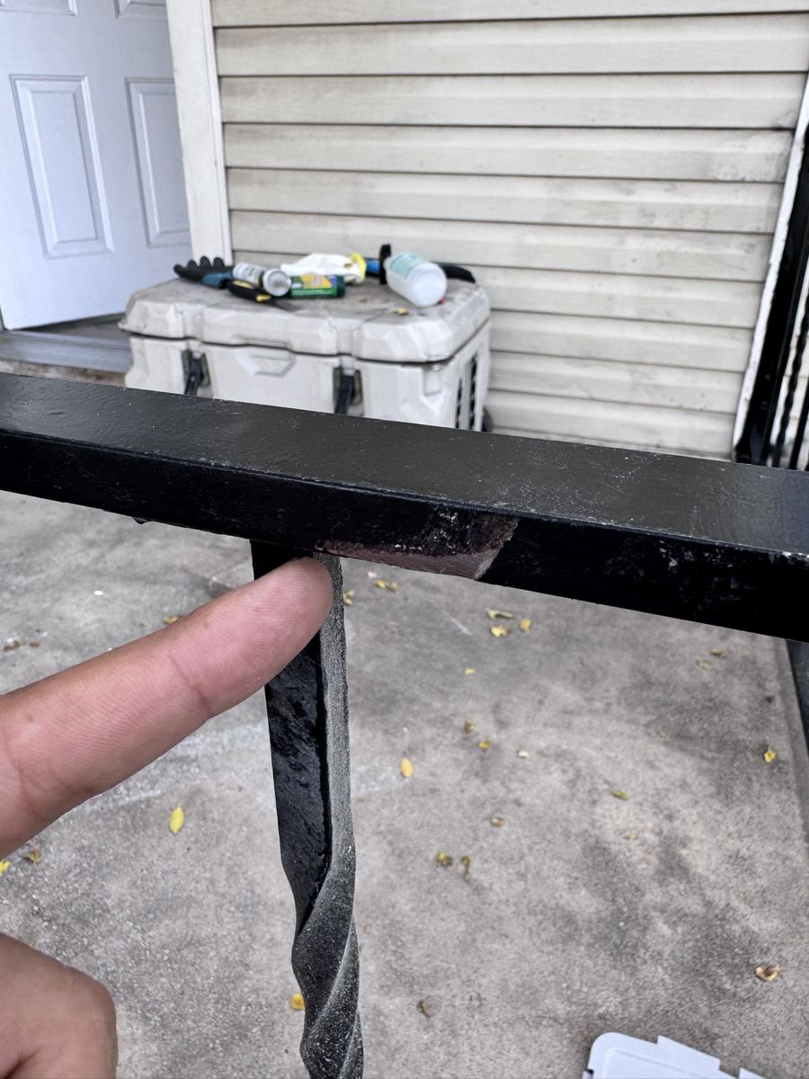 Close-up of a black handrail with a chipped, rusted spot at the joint where a baluster meets the top rail