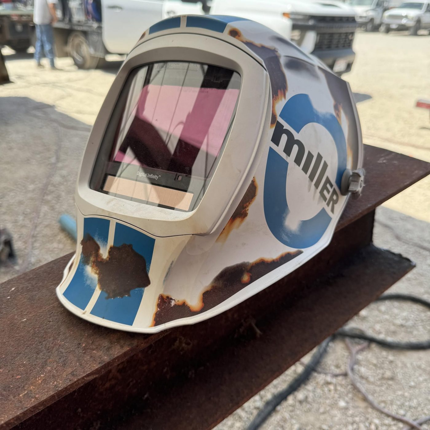 A white and blue welding helmet resting on a rusted steel beam at a job site