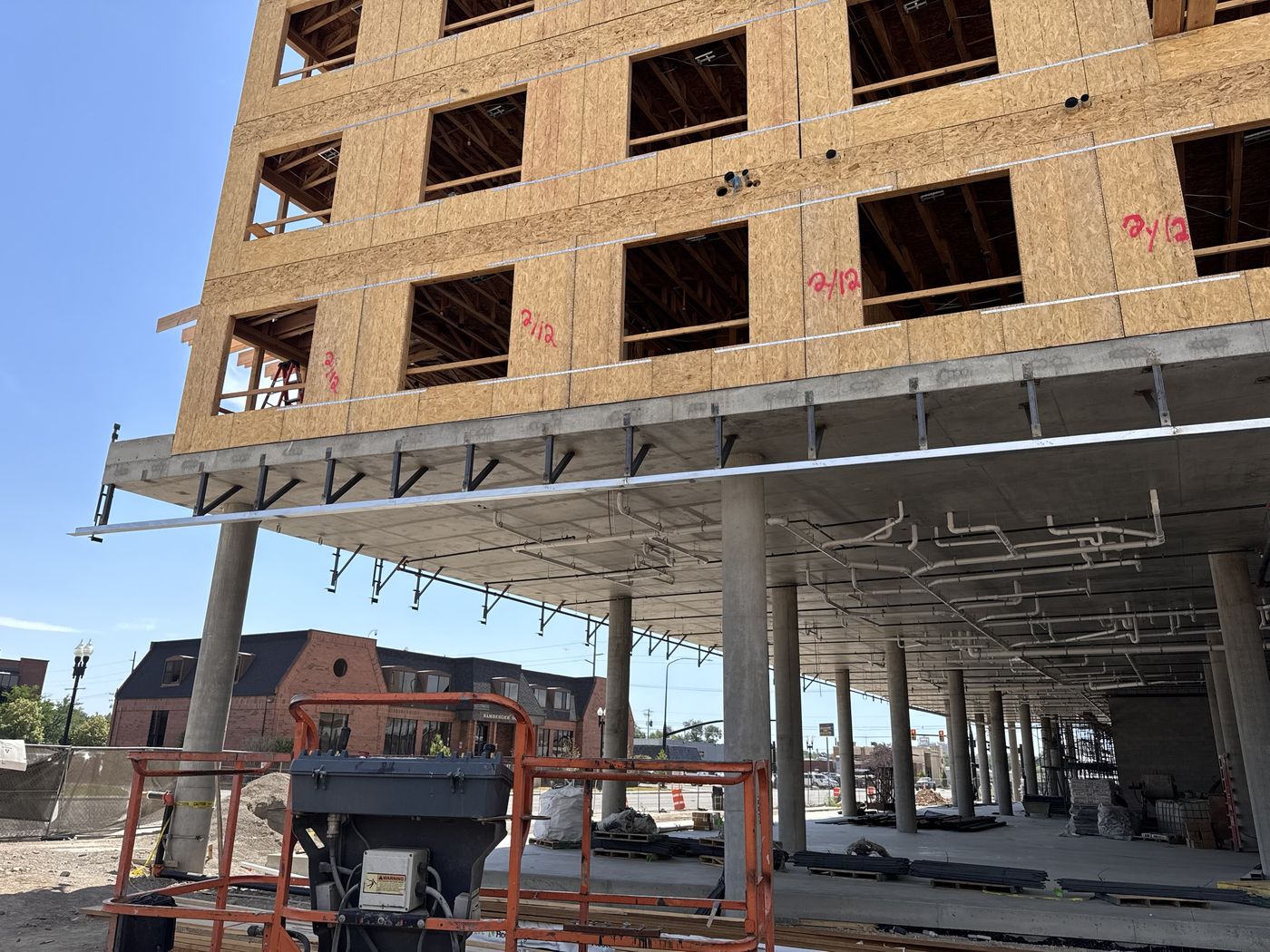Row of steel brackets and a ledger angle running along the edge of a concrete podium under a wood-framed building