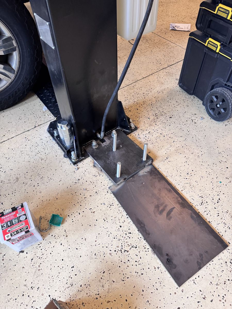 A steel base plate with threaded anchor rods laid out beside a lift column, ready to be welded
