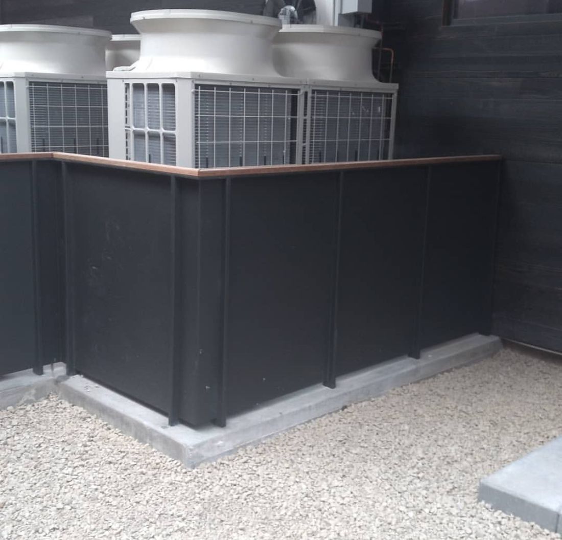 The finished black steel screen wall around the condenser units, topped with a wood cap rail